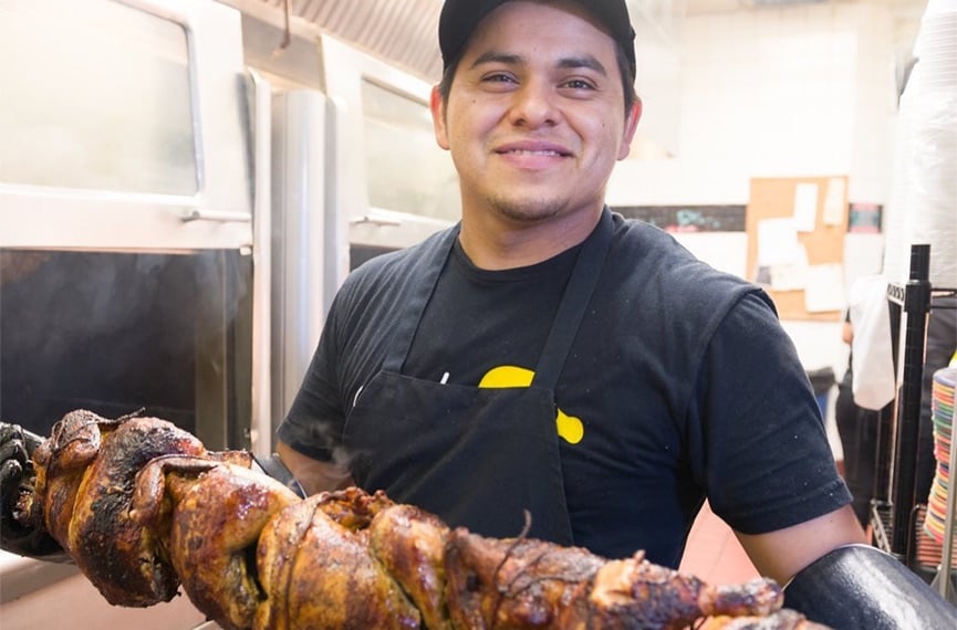 Man holding large skewer of cooked chicken